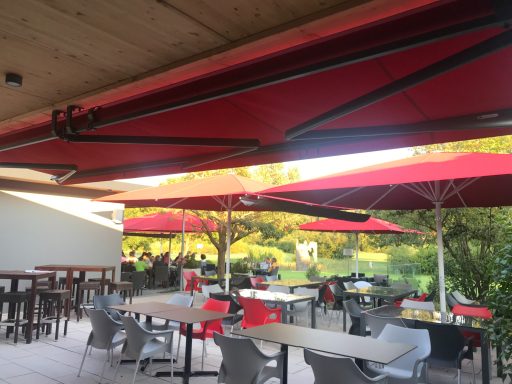 Markise und Sonnenschirme in rot auf einer Terrasse
